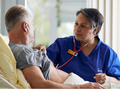 Sue Ryder nurse using a stethoscope to examine a patient in bed while providing hospice care.